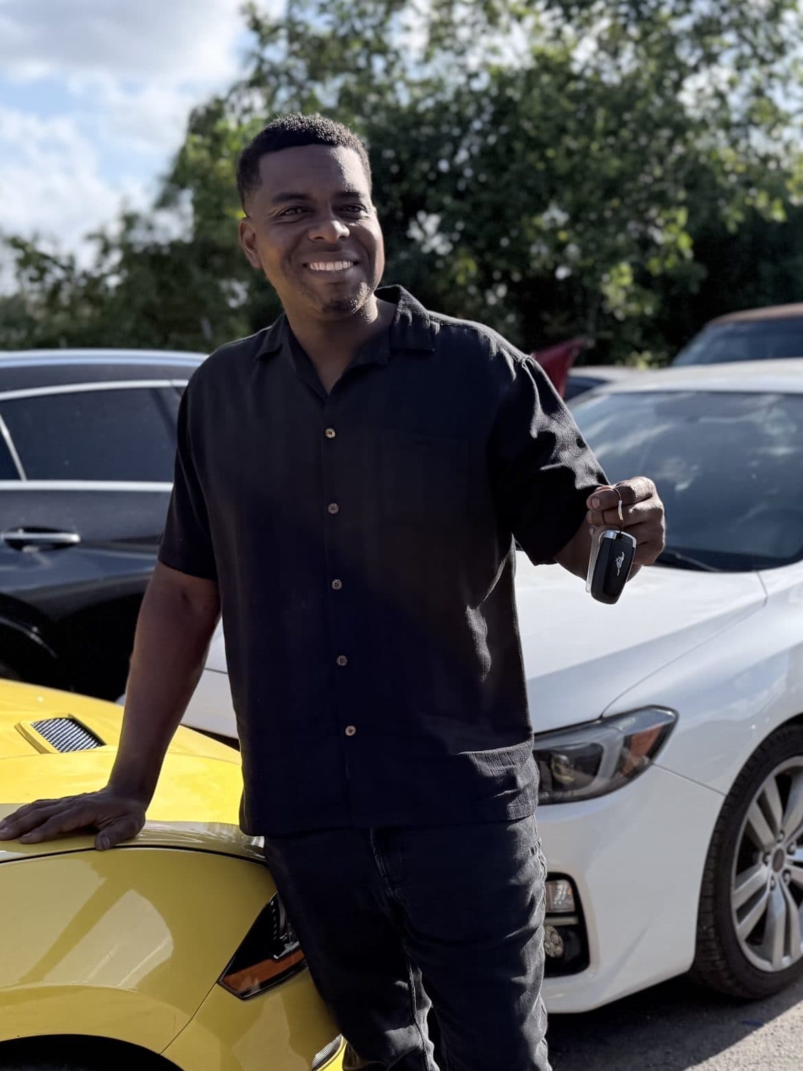 Omari Grant, ASE-certified mechanic and owner of Fort Lauderdale Auto Sales, holding car keys beside inspected inventory vehicles